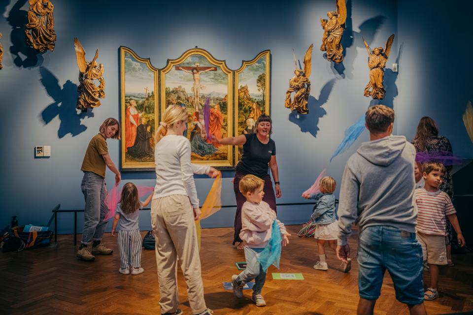 Kinderen en volwassenen gooien met slingers in een museumzaal.
